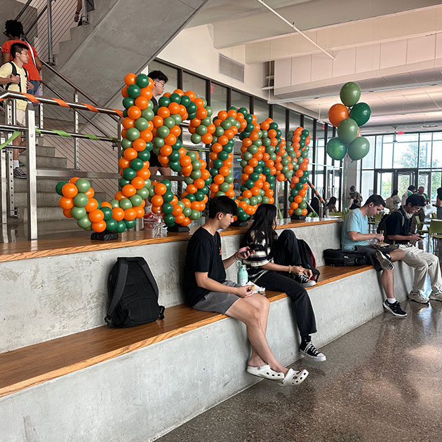 Students sit by the balloon JSOM sign.