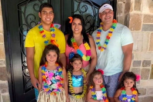 JSOM Alum Jessica Gonzalez stands in front of a door with her family, all wearing multicolored leis