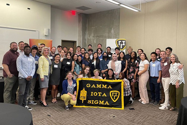 Gamma Iota Sigma members in UT Dallas JSOM's chapter gather behind their banner.