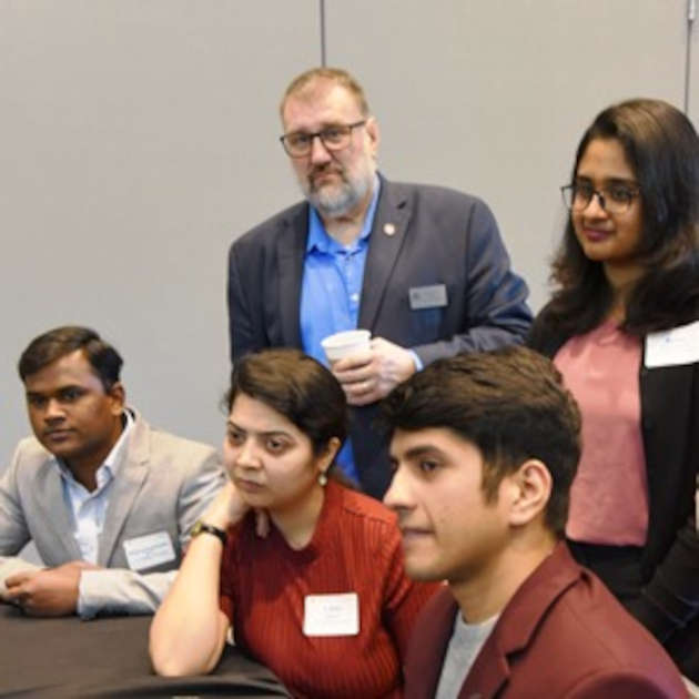 William (Bill) Hefley, (standing, at left) with students at an information technology symposium in February